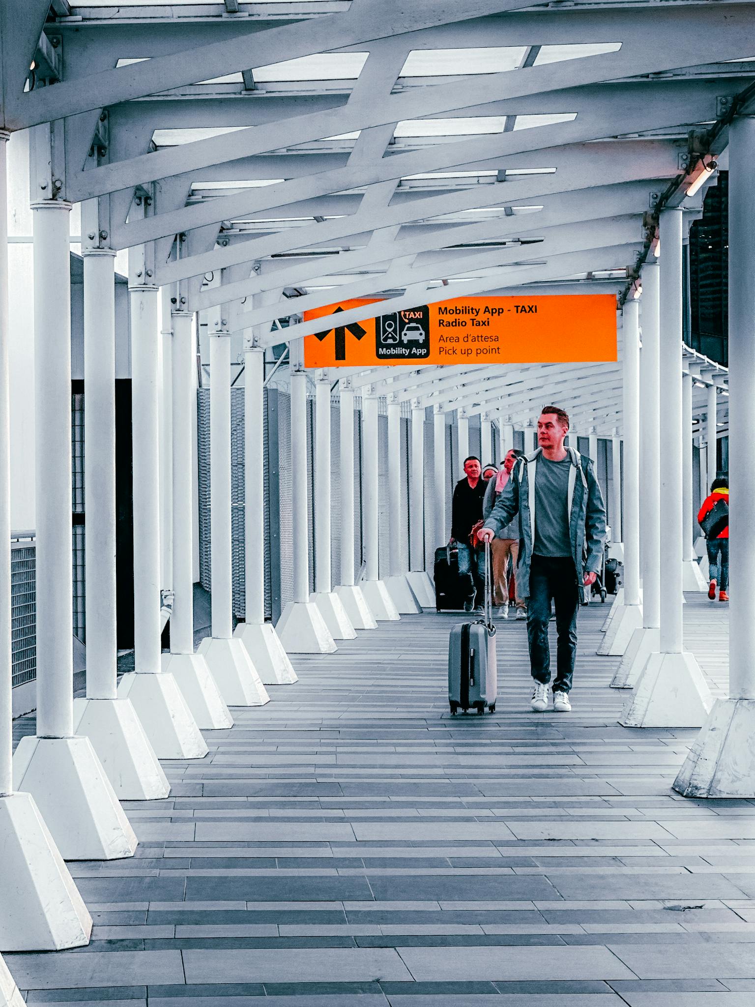Travelers walking through a modern airport walkway with luggage, heading towards a taxi pickup point.